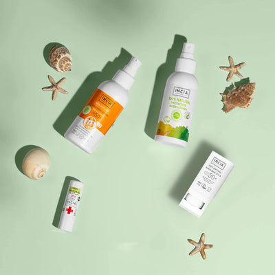 Flat lay of the INCIA Sun & Summer Family Set on a green background with shells and starfish: sunscreen lotion, insect bite remedy, sunscreen stick and SOS Stick